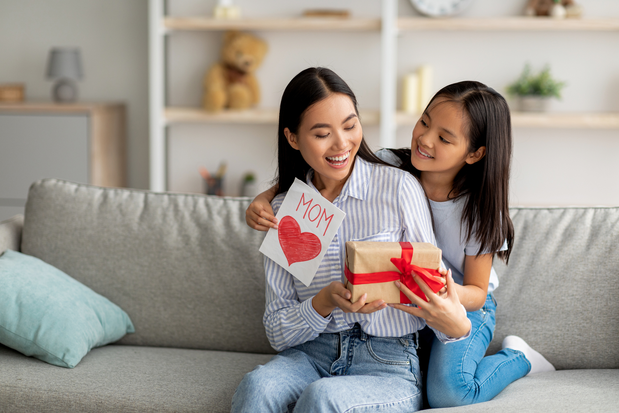 Congratulations. Loving asian daughter greeting surprised mom with Mother's Day, giving her handmade card and gift box