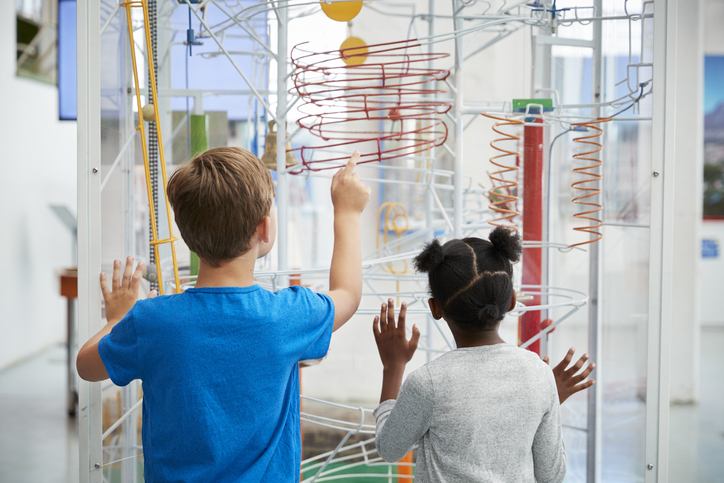 Two kids looking at a science exhibit,  back view